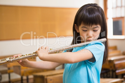 Cute pupil playing flute in classroom