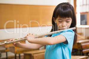 Cute pupil playing flute in classroom