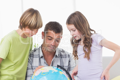 Siblings with father exploring map on globe