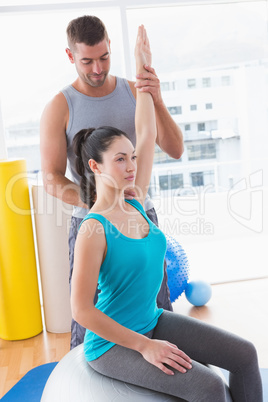 Trainer assisting woman exercising on fitness ball