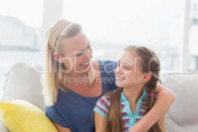 Happy mother and daughter sitting on sofa at home