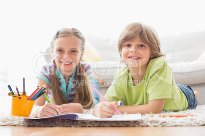 Portrait of happy siblings drawing while lying on rug