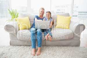 Happy mother and daughter using laptop on sofa