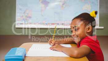 Cute little girl writing book in classroom