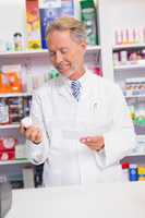 Smiling senior pharmacist holding prescription and jar