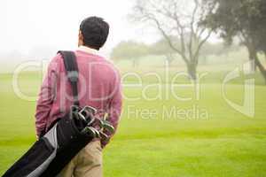 Golfer walking and holding his golf bags
