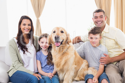 Happy family sitting with Golden Retriever on sofa