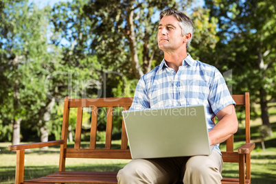 Man sitting on park bench using laptop