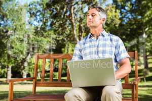 Man sitting on park bench using laptop