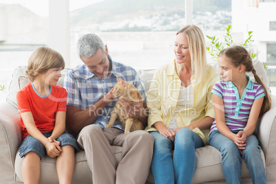 Family sitting with cat on sofa at home