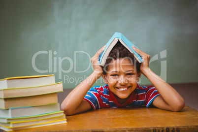 Little boy holding book over head in classroom