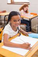 Cute pupils drawing at their desks one smiling at camera