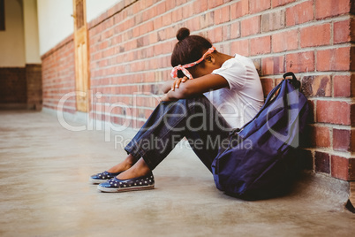 Tensed girl sitting against brick wall in school corridor