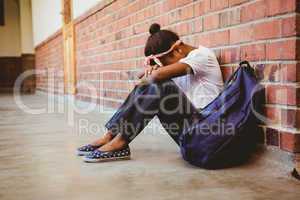 Tensed girl sitting against brick wall in school corridor