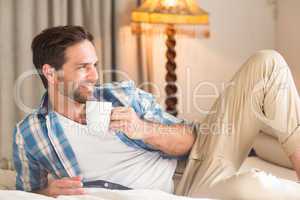 Handsome man relaxing on his bed with hot drink