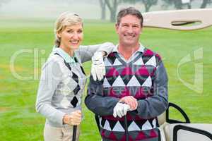 Happy golfing couple with golf buggy behind