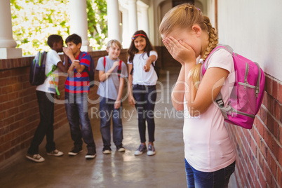 Sad schoolgirl with friends in background at school corridor