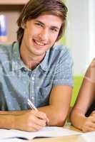 Happy male student doing homework in library