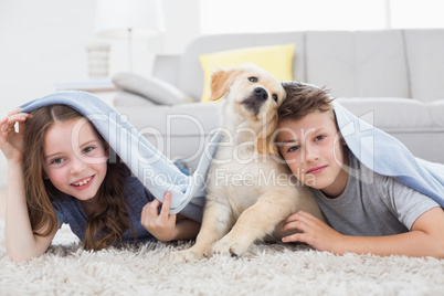 Cute siblings with dog under blanket in living room
