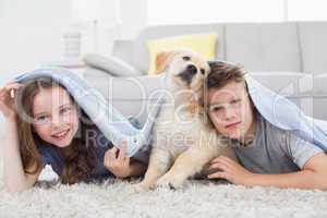 Cute siblings with dog under blanket in living room
