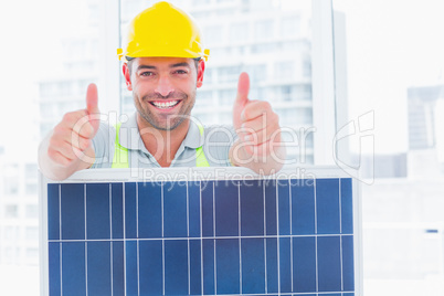 Smiling manual worker with solar panel gesturing thumbs up