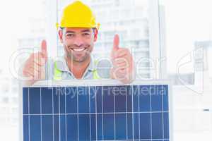 Smiling manual worker with solar panel gesturing thumbs up