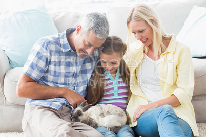 Parents and daughter playing with rabbit at home