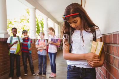 Sad schoolgirl with friends in background at school corridor