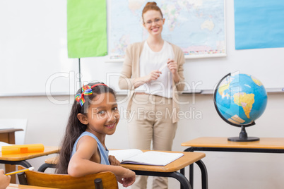 Cute pupil and teacher in classroom with globe