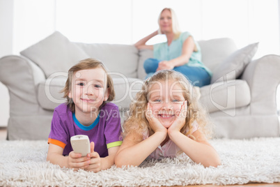 Happy children lying on rug while woman sitting on sofa