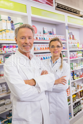 Smiling pharmacist and his trainee with arms crossed