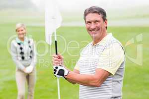 Happy golfer holding flag for cheering partner