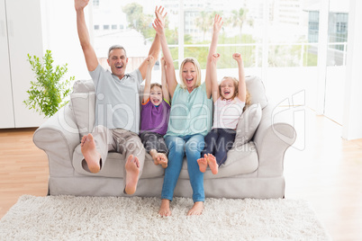 Family of four with arms raised sitting on sofa