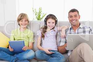 Happy man with children using technologies on sofa