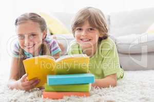 Happy siblings reding book while lying on rug