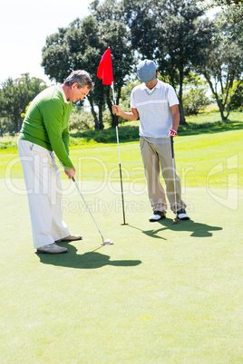 Golfer holding hole flag for friend putting ball