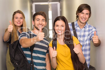 Happy students gesturing thumbs up at college corridor