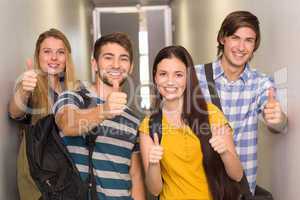 Happy students gesturing thumbs up at college corridor