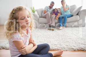 Upset girl sitting on floor while parents enjoying with brother