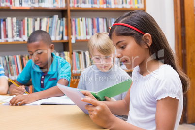 Cute pupils writing at desk in library