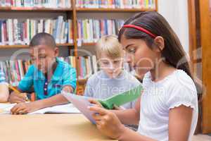 Cute pupils writing at desk in library