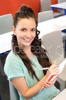 Smiling female student writing notes in classroom