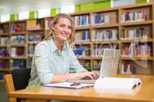 Pretty student studying in the library with laptop