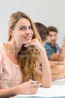 Smiling female student writing notes in classroom