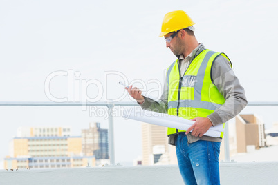 Architect with blueprints reading clipboard outdoors