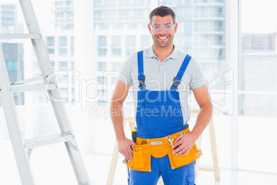 Smiling repairman in overalls at bright office