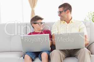 Father and son looking at each other while using laptop
