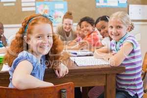 Cute pupils writing at desk in classroom