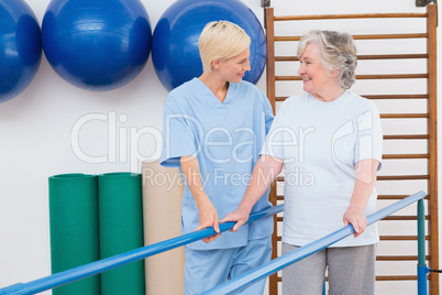 Therapist helping senior woman to walk with parallel bars