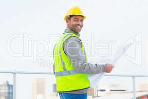 Architect in protective clothing holding blueprint outdoors